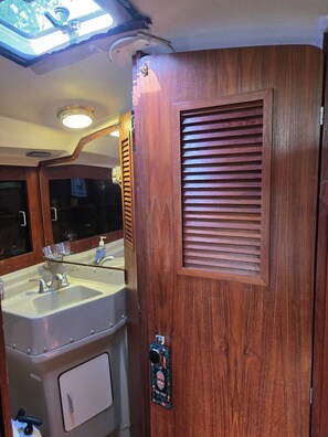 A bathroom with a wooden door, a sink, and a mirror. -  3-Bed Yacht in Muskegon w/ Sail Kayaks \& Beach Trail/AC/Heat/wireless internet (Muskegon)
