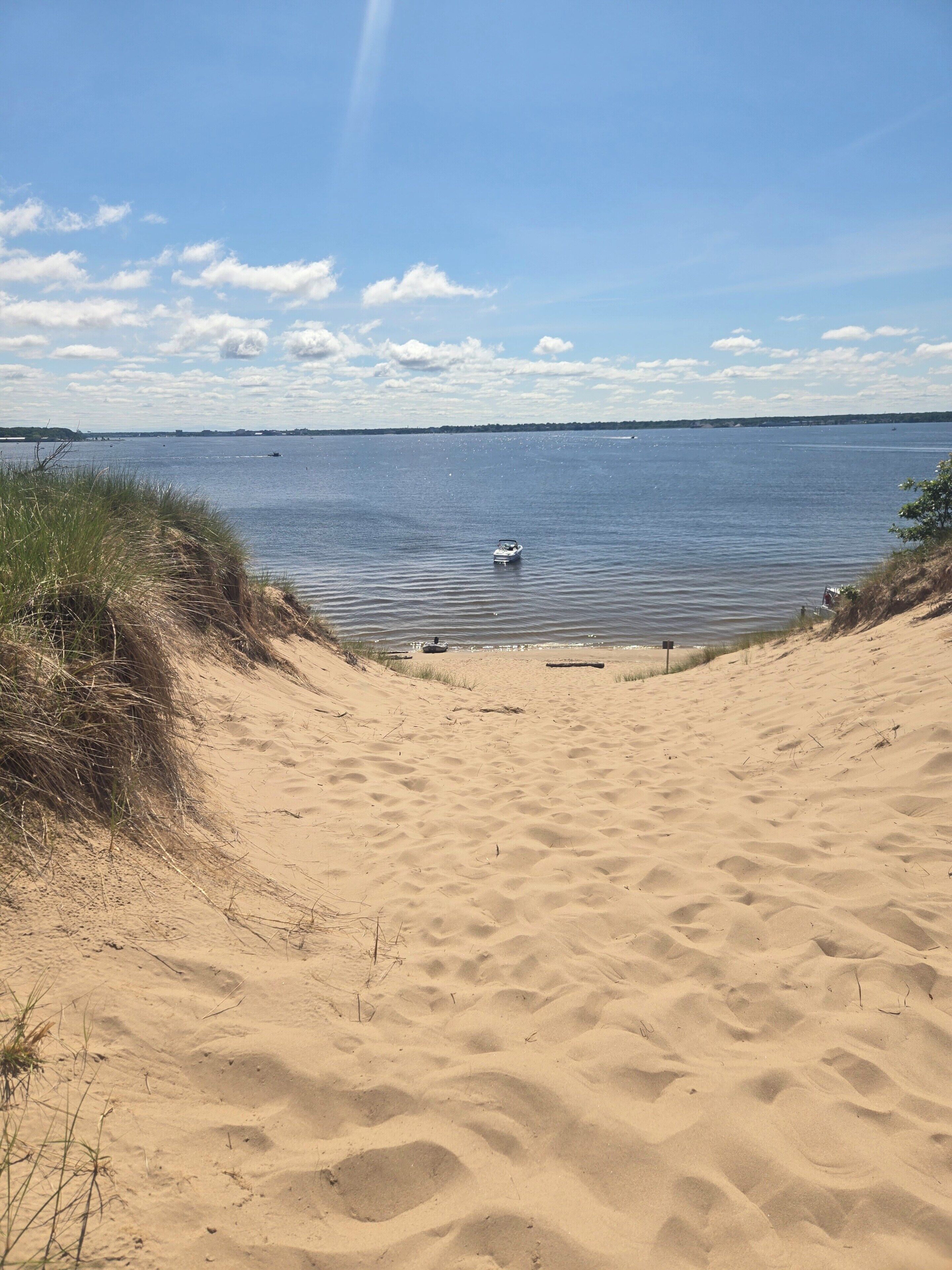 A sandy beach leading to calm water with a boat in the distance.