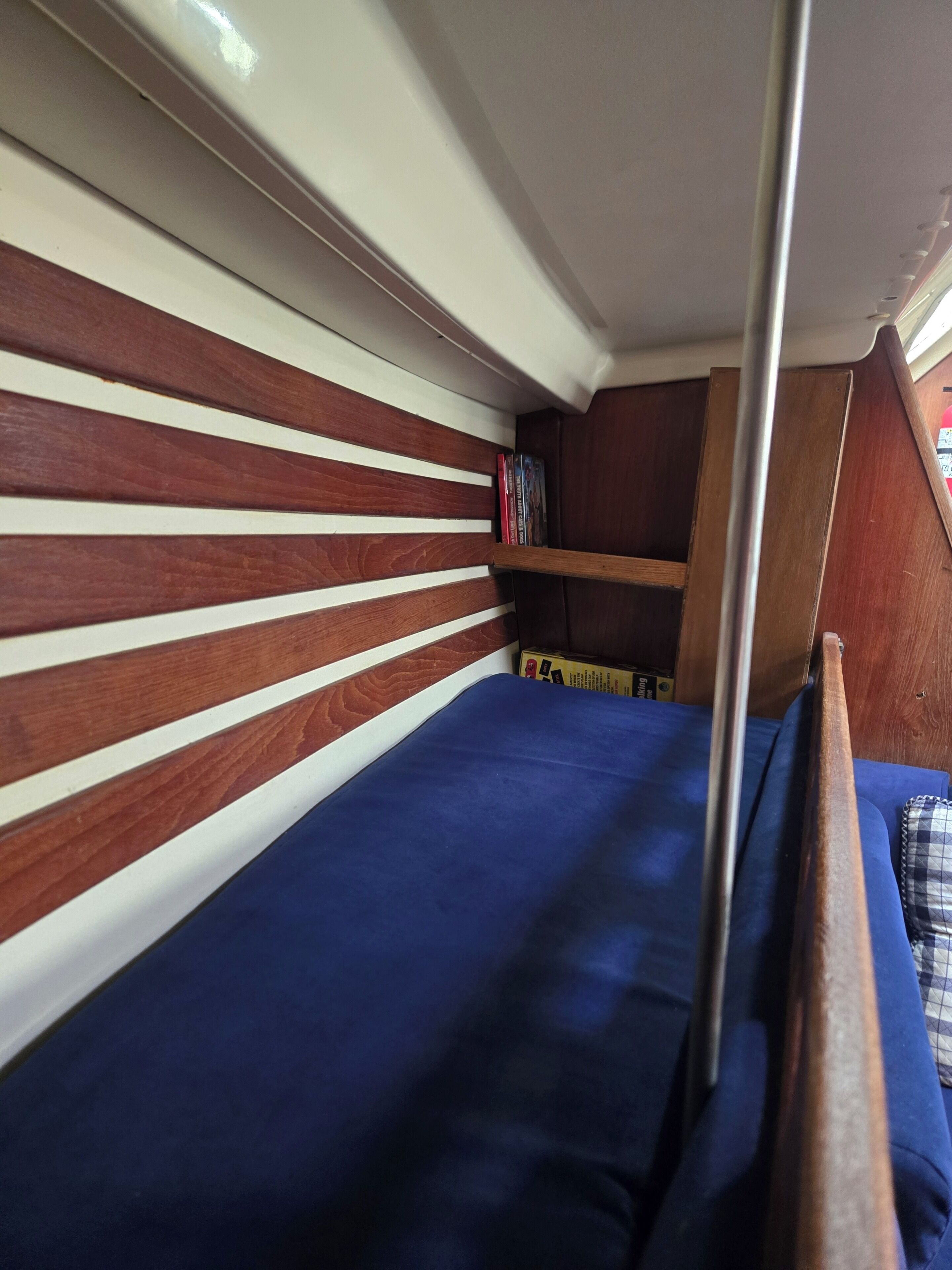 Una cama litera con colchón azul, listones de madera en la cabecera y una estantería con libros.