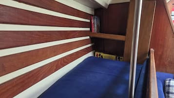Una cama litera con colchón azul, listones de madera en la cabecera y una estantería con libros.