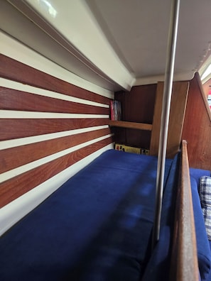 Una cama litera con colchón azul, listones de madera en la cabecera y una estantería con libros.