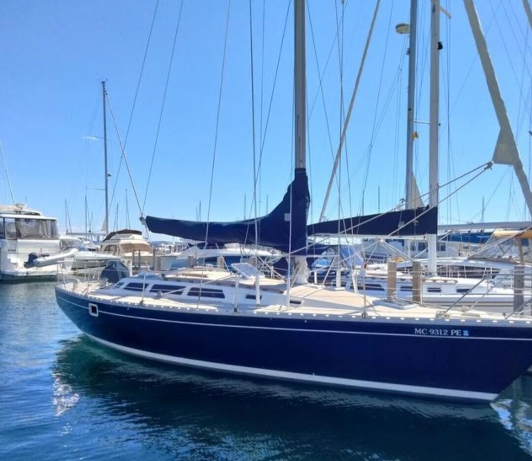 A sailboat docked at a marina with other boats, clear skies, and calm water.