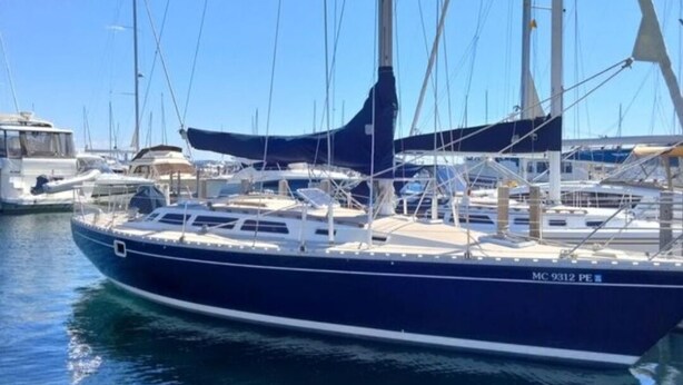 Un'imbarcazione a vela ormeggiata in una marina, con altre barche, cielo sereno e acqua calma.