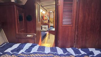 Een slaapkamer met een bed, een houten garderobe en een zithoekje met een kussen.