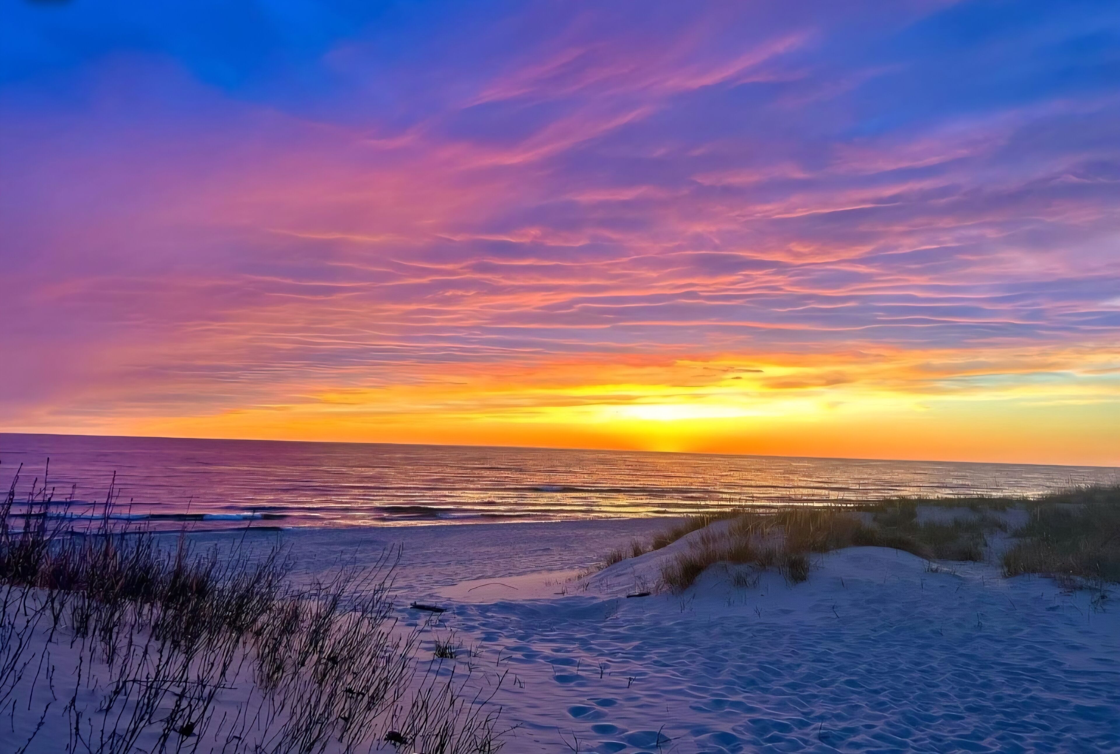 A beach with sand dunes and a sunset over the ocean.
