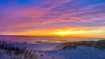 Een strand met duinen en een zonsondergang boven de oceaan.
