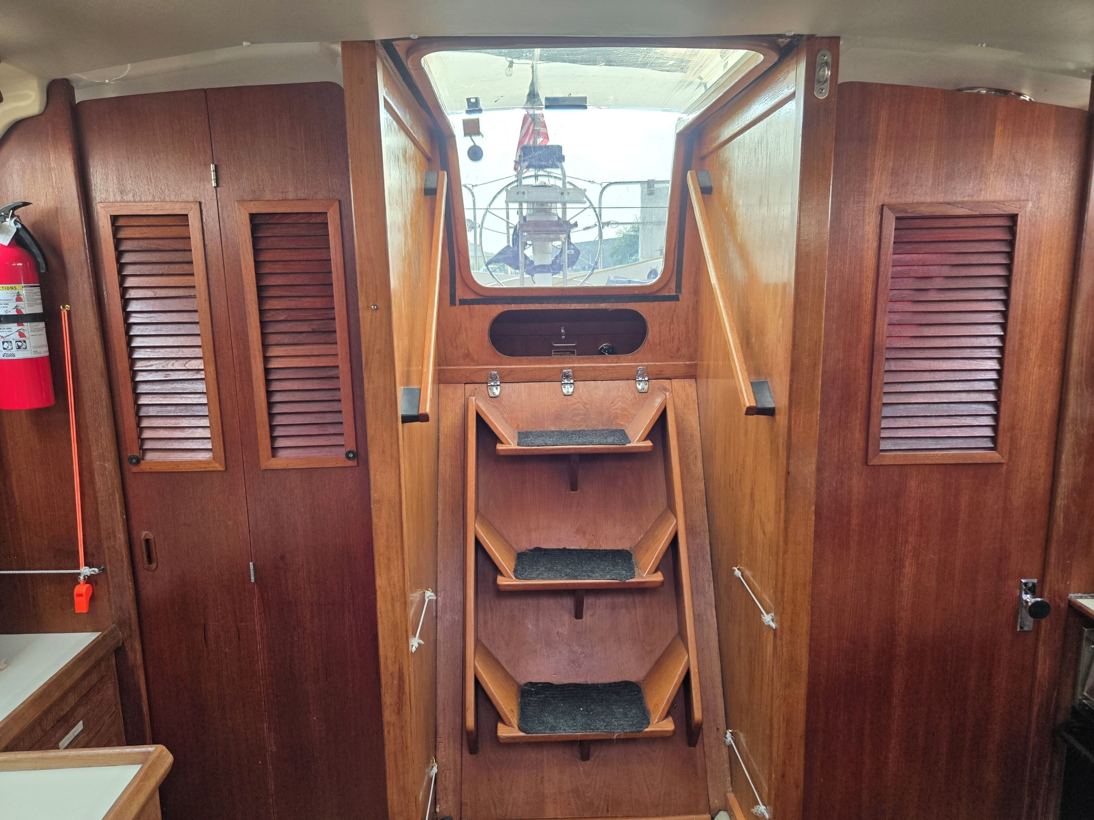 Interior de madera con una ventana, un extintor y una escalera.