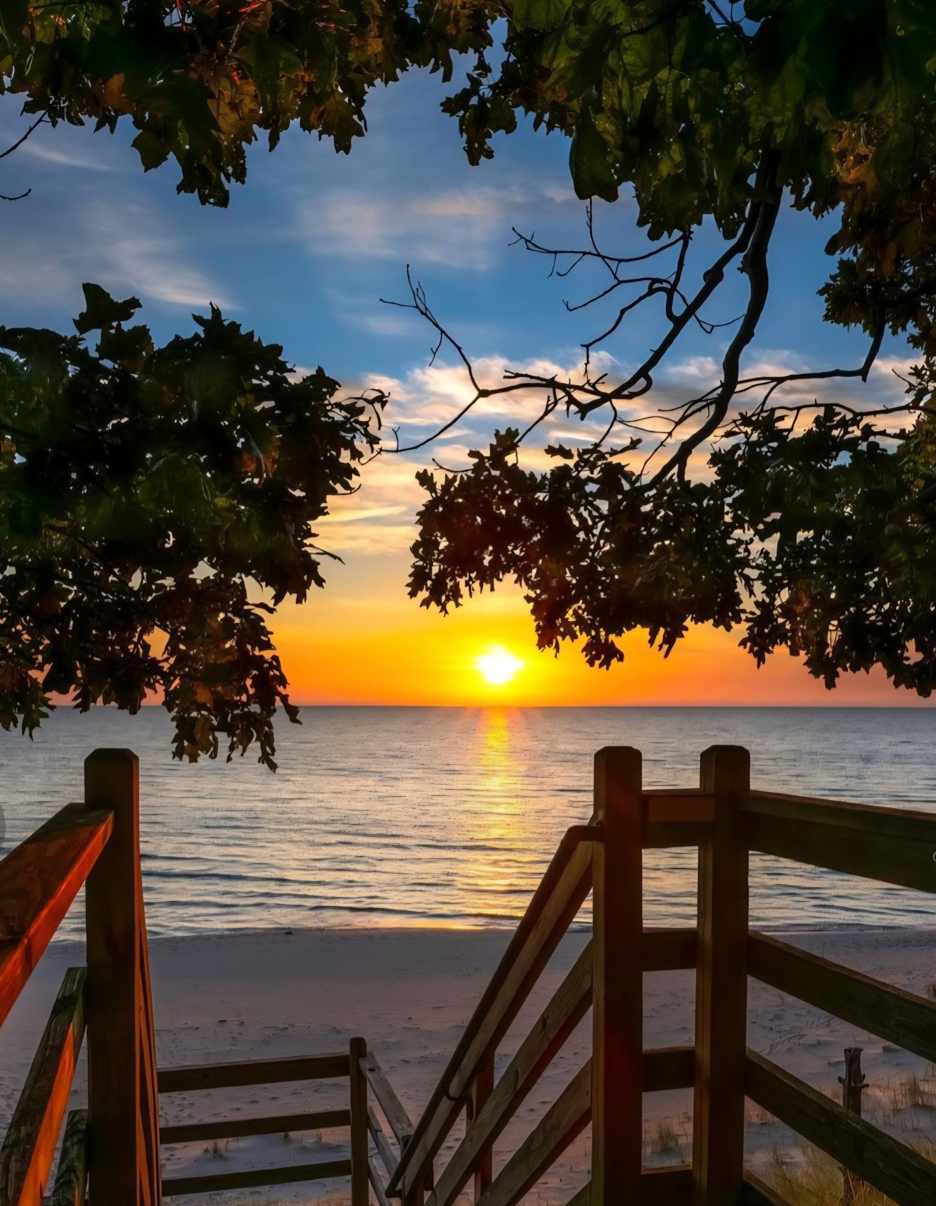 A wooden deck leading to a beach with a sunset in the background.