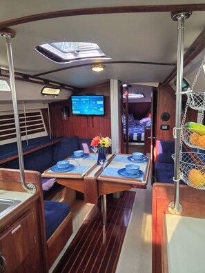 A dining area with a table set for two, a television mounted on the wall, and a seating area with a view of the outdoors. -  3-Bed Yacht in Muskegon w/ Sail Kayaks \& Beach Trail/AC/Heat/wireless internet (Muskegon)