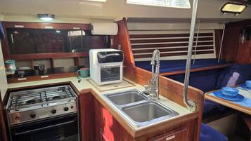 Een kleine keuken met een kookplaat, oven, spoelbak en een kleine koelkast.