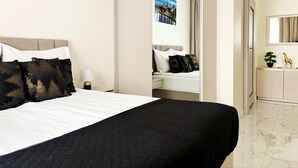 A hotel room with a bed, a nightstand, a lamp, a mirror, a dresser, and a view of a cityscape. - MARGI Liva Apartament (Szczecin)
