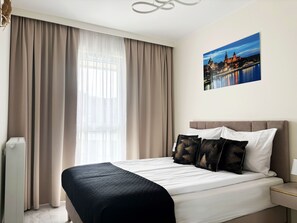 A hotel room with a bed, curtains, a nightstand, and a wall-mounted picture. - MARGI Liva Apartament (Szczecin)