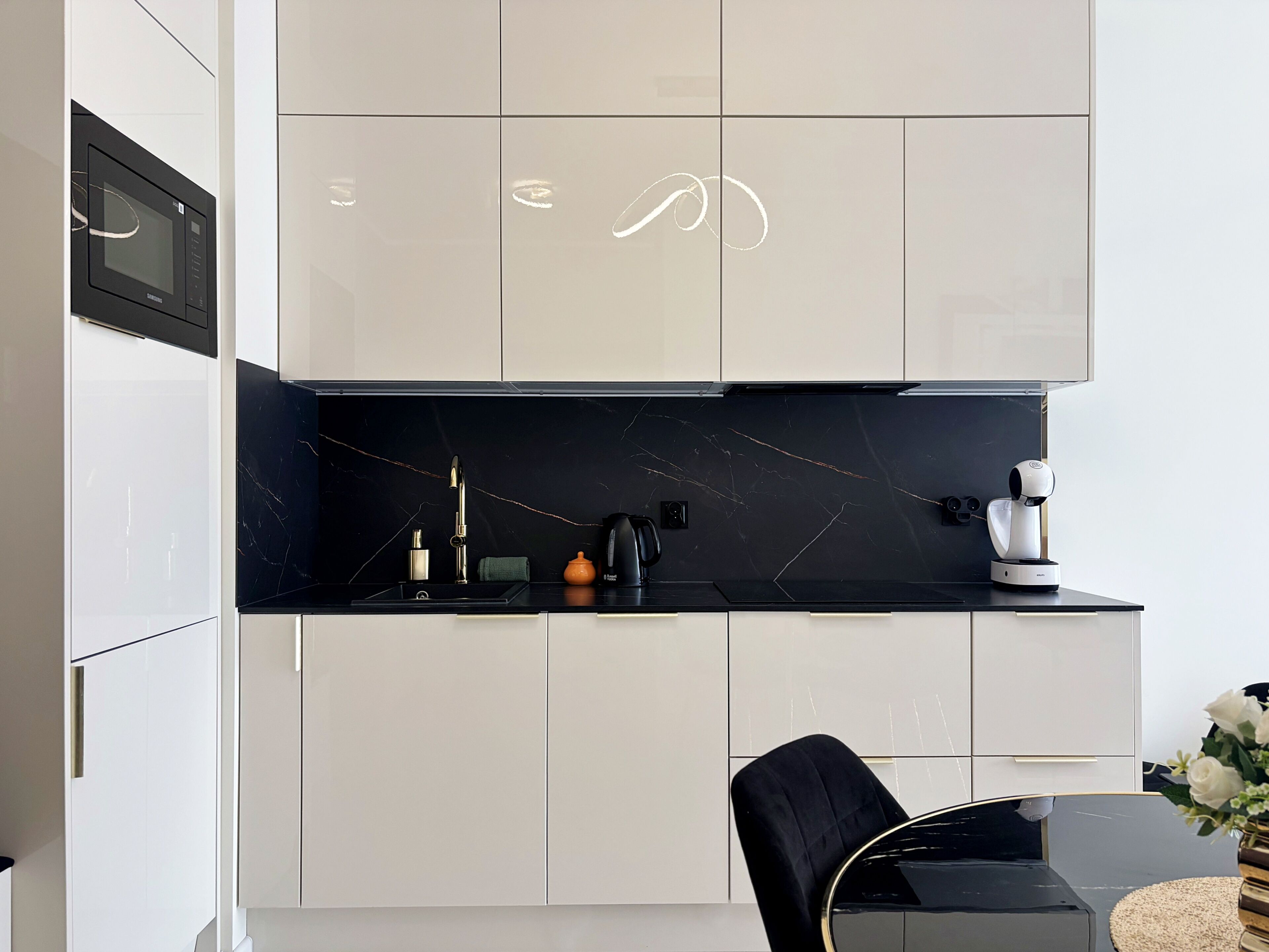 A modern kitchen with white cabinets, a black countertop, and a black chair.