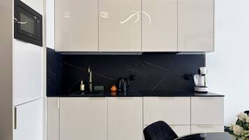 A modern kitchen with white cabinets, a black countertop, and a black chair.