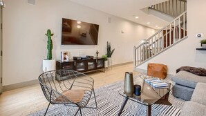 Ein modernes Wohnzimmer mit Flachbildfernseher, einer Treppe und einem Essbereich mit Glastisch.