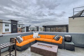 Eine Dachterrasse mit Ecksofa, Feuerstelle und einem kleinen Tisch mit einem Korb.