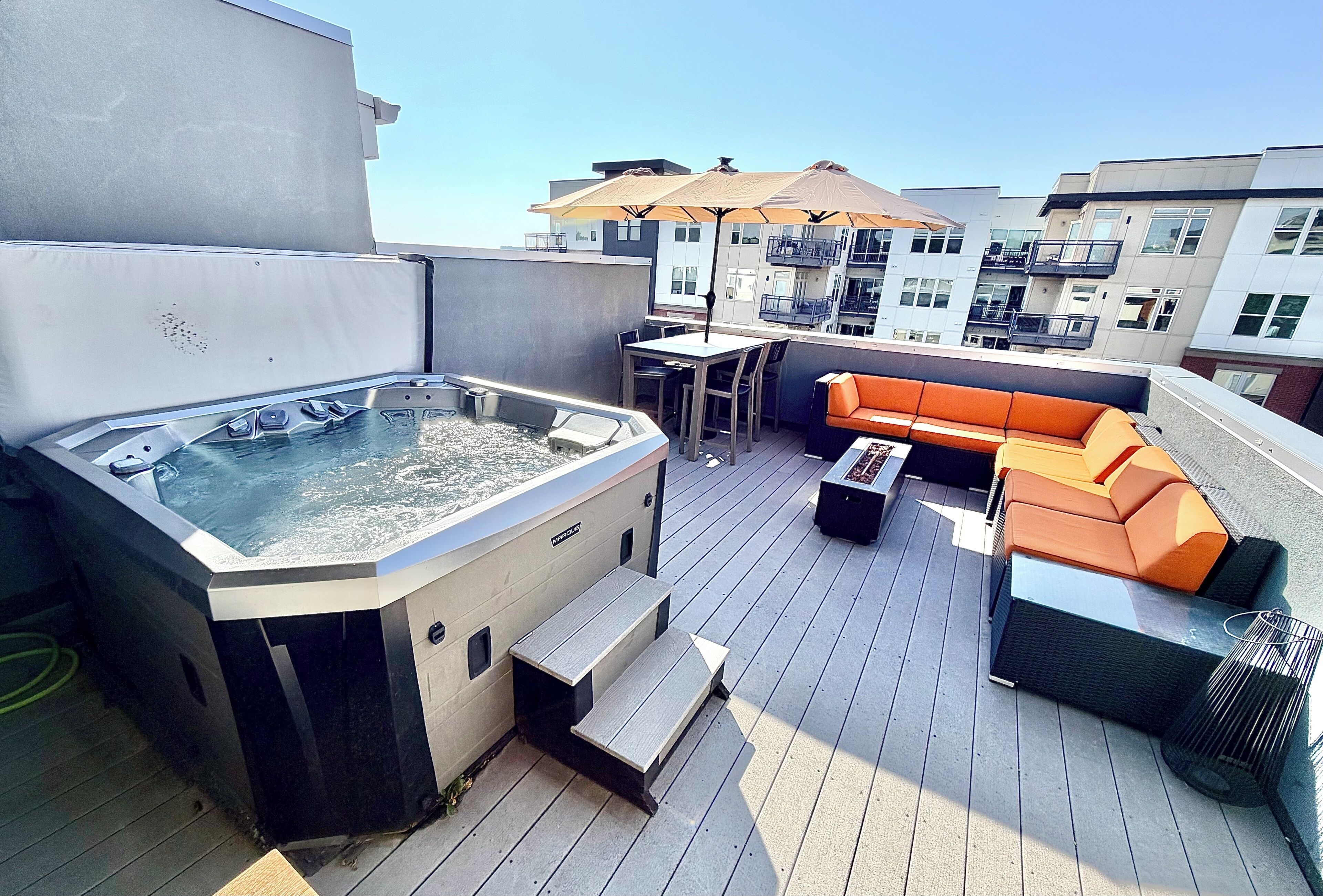 Een terras op het dak met een hottub, buitenmeubels en een tafel.