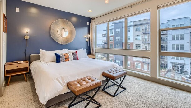 Ein Schlafzimmer mit einem großen Bett, einem runden Spiegel, Nachttischlampen, einem Fenster mit Blick auf die Stadt und einer kleinen Holzbank.