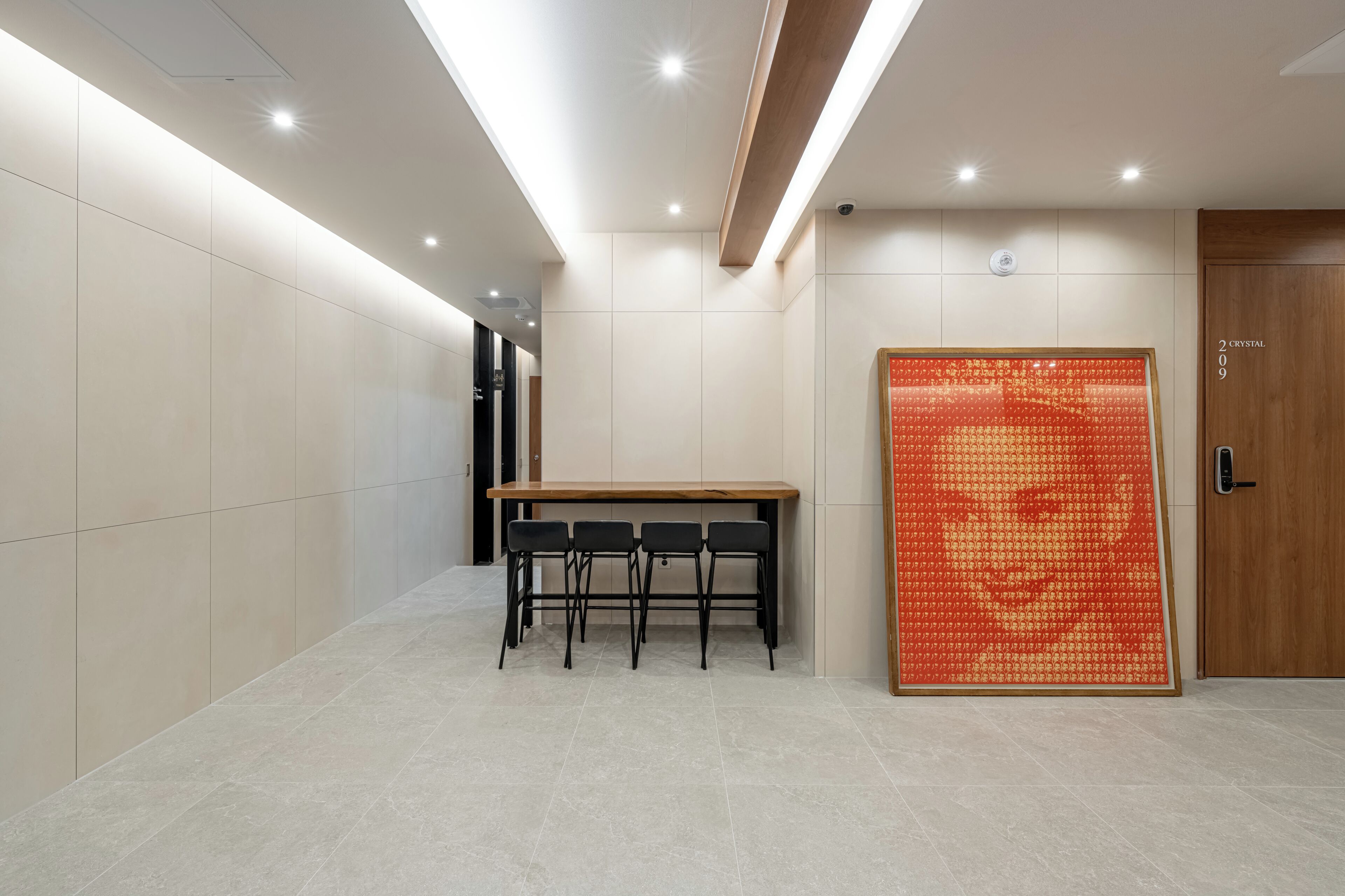 Un pasillo con una mesa, sillas, una puerta con número y un papel tapiz decorado.