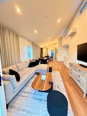 A modern living room with a sofa, coffee table, and TV stand. - Luxury Lenah Valley Retreat, Minutes to MONA & CBD (Lenah Valley)