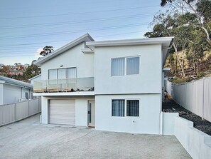Ein zweistöckiges Wohngebäude mit Garage, Balkon und umzäunter Garten.