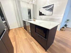 Una cocina moderna con lavavajillas integrado, un lavamanos de acero inoxidable y una isla grande con encimera blanca.