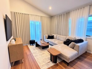 A modern living room with a sofa, a coffee table, a TV, and a window with curtains. - Luxury Lenah Valley Retreat, Minutes to MONA & CBD (Lenah Valley)