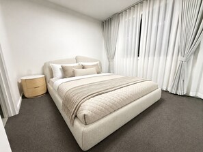 Un dormitorio moderno con una cama grande, una mesita de noche y un ventanal con cortinas.