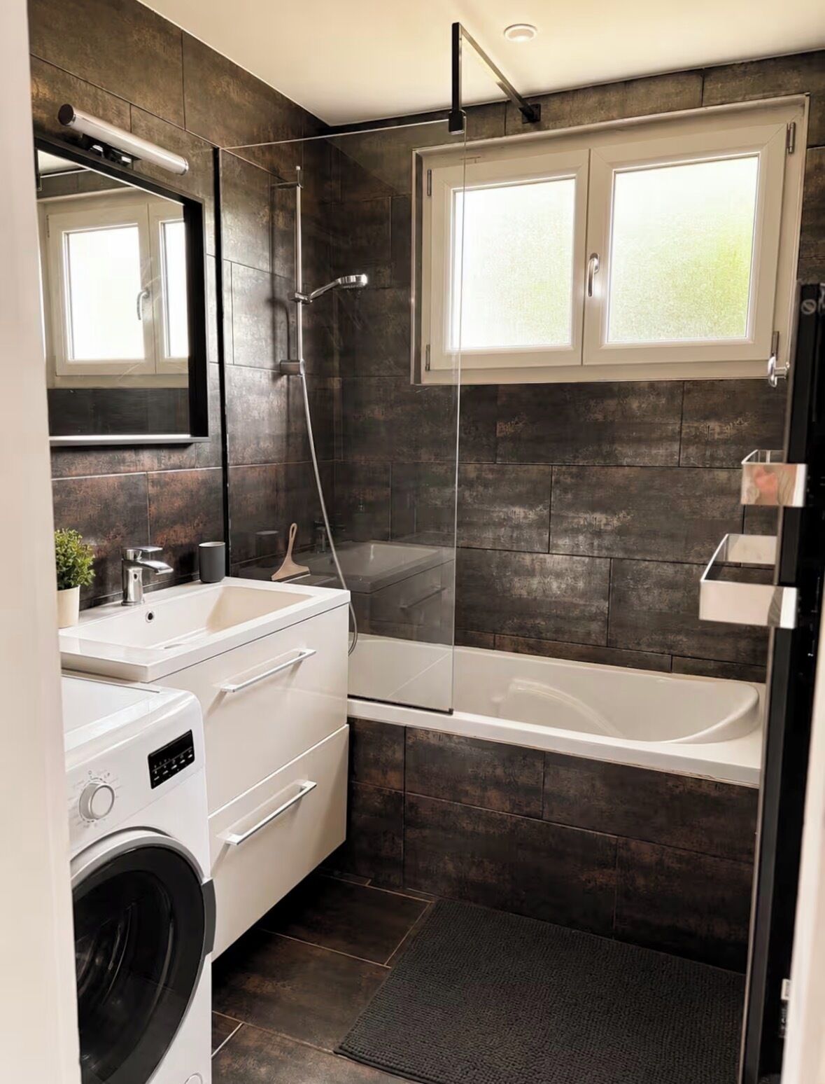 A modern bathroom with a built-in washing machine, a bathtub, and a glass shower enclosure.
