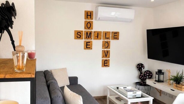 A modern living room with a grey sofa, a coffee table, a TV, and a wall with a 'HOME SMILE' decoration. - Apartments in the Vosges (Fresse-sur-Moselle)