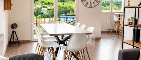 A modern living room with a dining area, large windows, and a view of greenery.