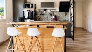 A modern kitchen with a wooden bar, white bar stools, a TV, and a marble backsplash. - Apartments in the Vosges (Fresse-sur-Moselle)