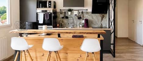 Une cuisine moderne avec un bar en bois, des tabourets de bar blancs, un téléviseur et un pare-feu en marbre.
