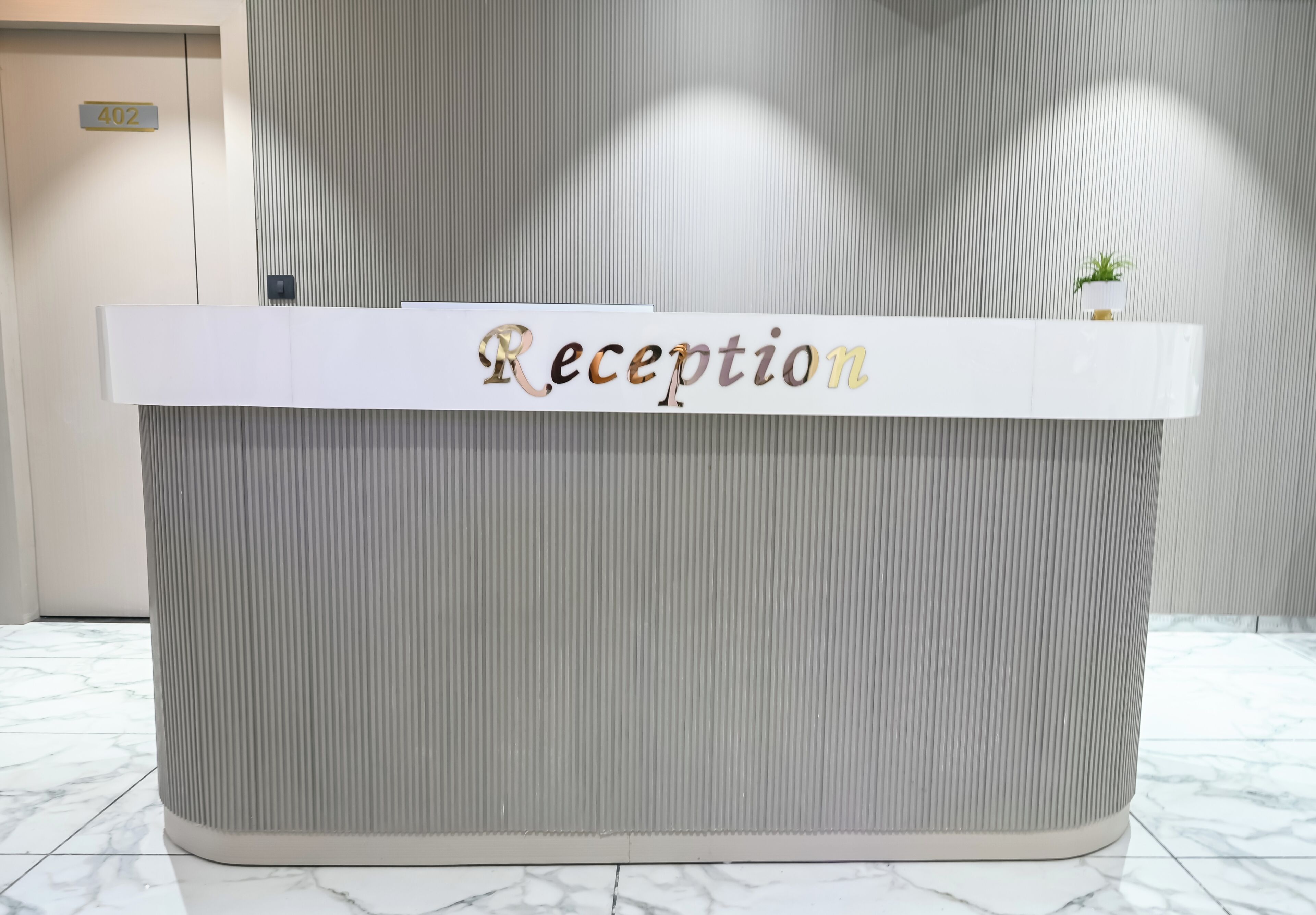Un mostrador de recepción con un letrero que dice 'Reception' y una pequeña planta encima.