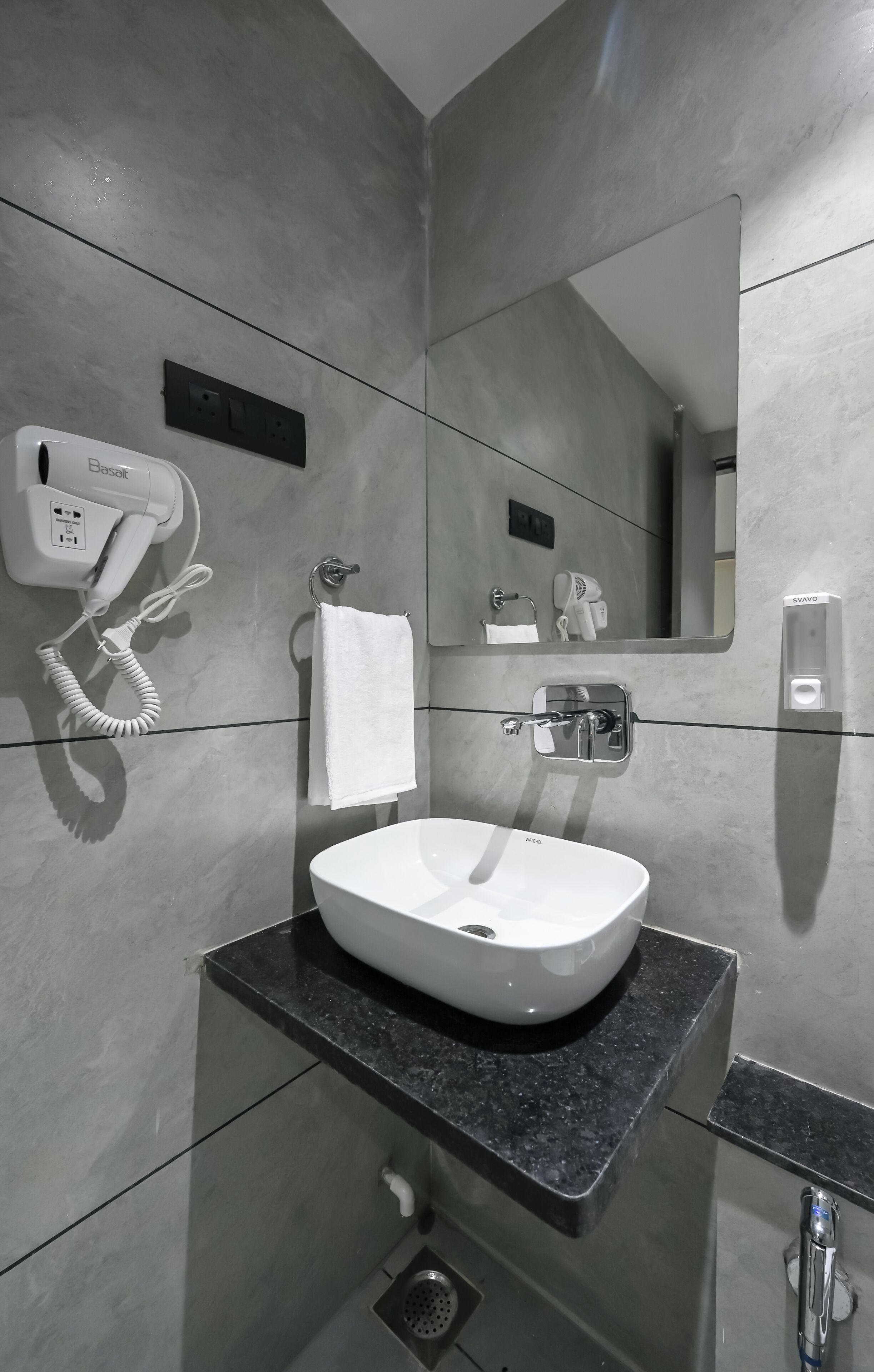 Ein modernes Badezimmer mit Waschbecken, Fön, Handtuchhalter, Spiegel und Seifenspender.