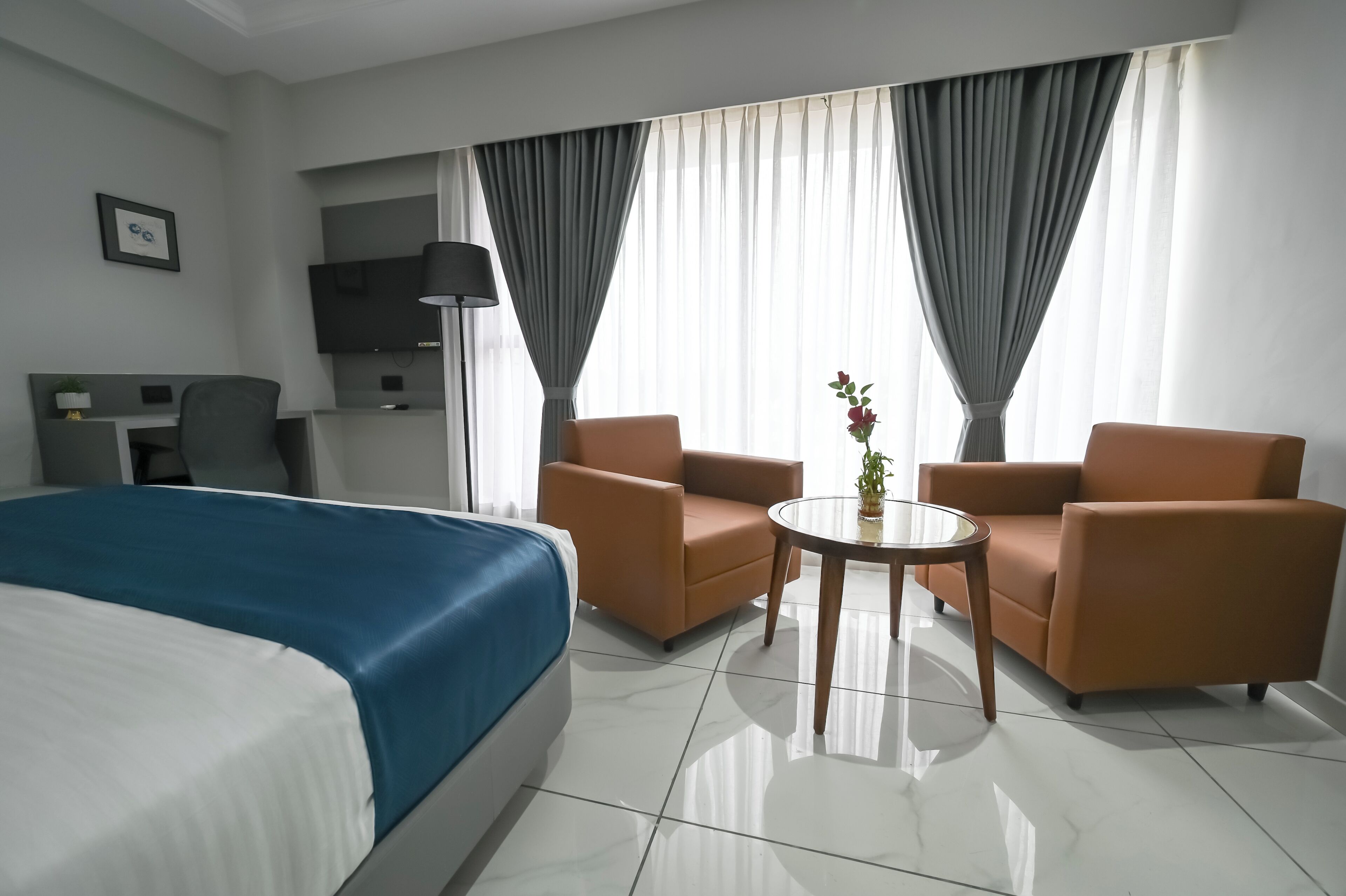 A hotel room with a bed, two armchairs, a small table, a TV, and curtains.