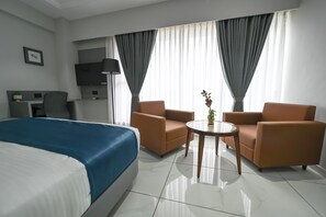Habitació d'hotel amb un llit, dos seients, una taula petita, una televisió i cortines.