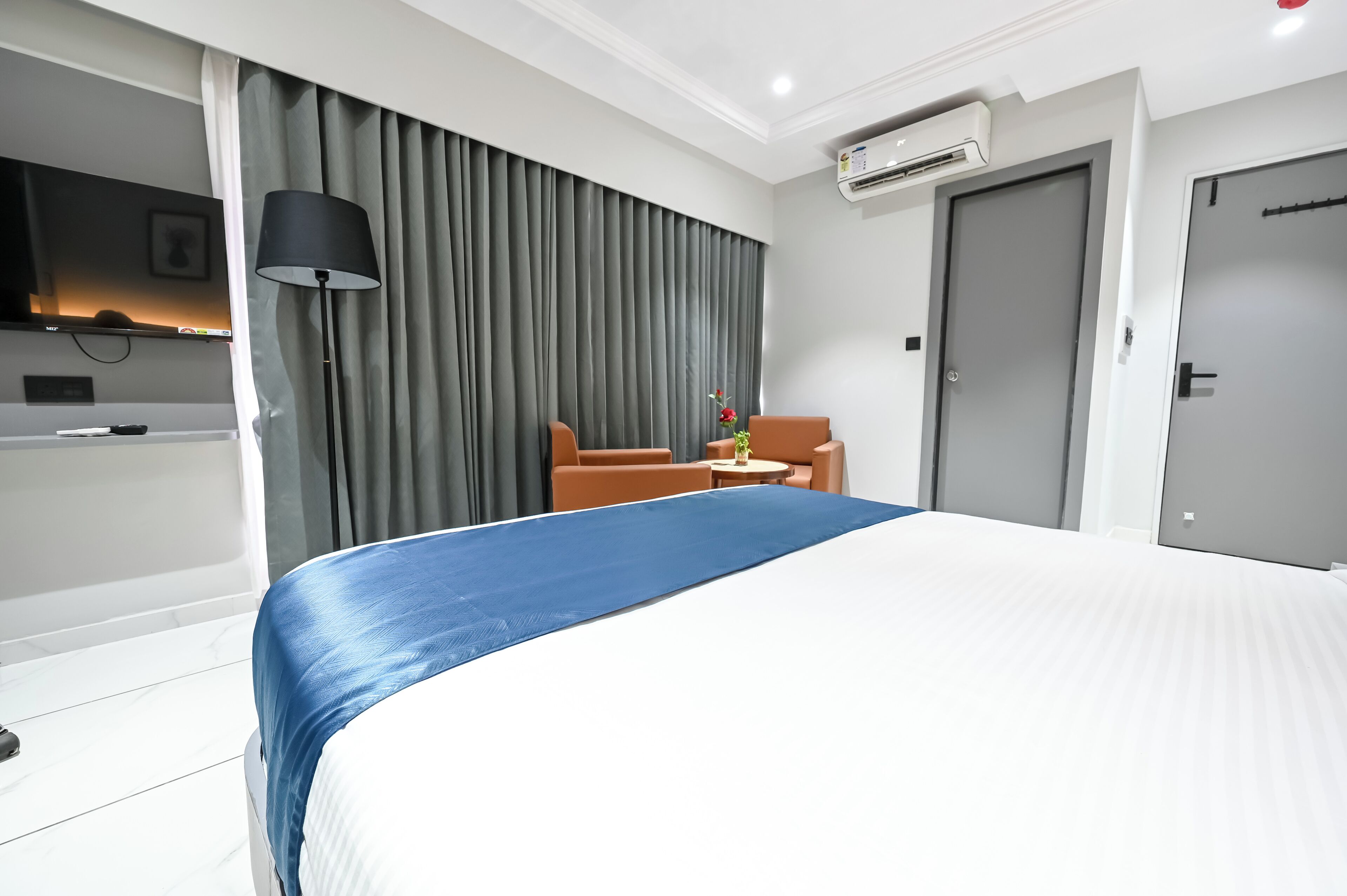A hotel room with a bed, a chair, a table, an air conditioning unit, and a door.