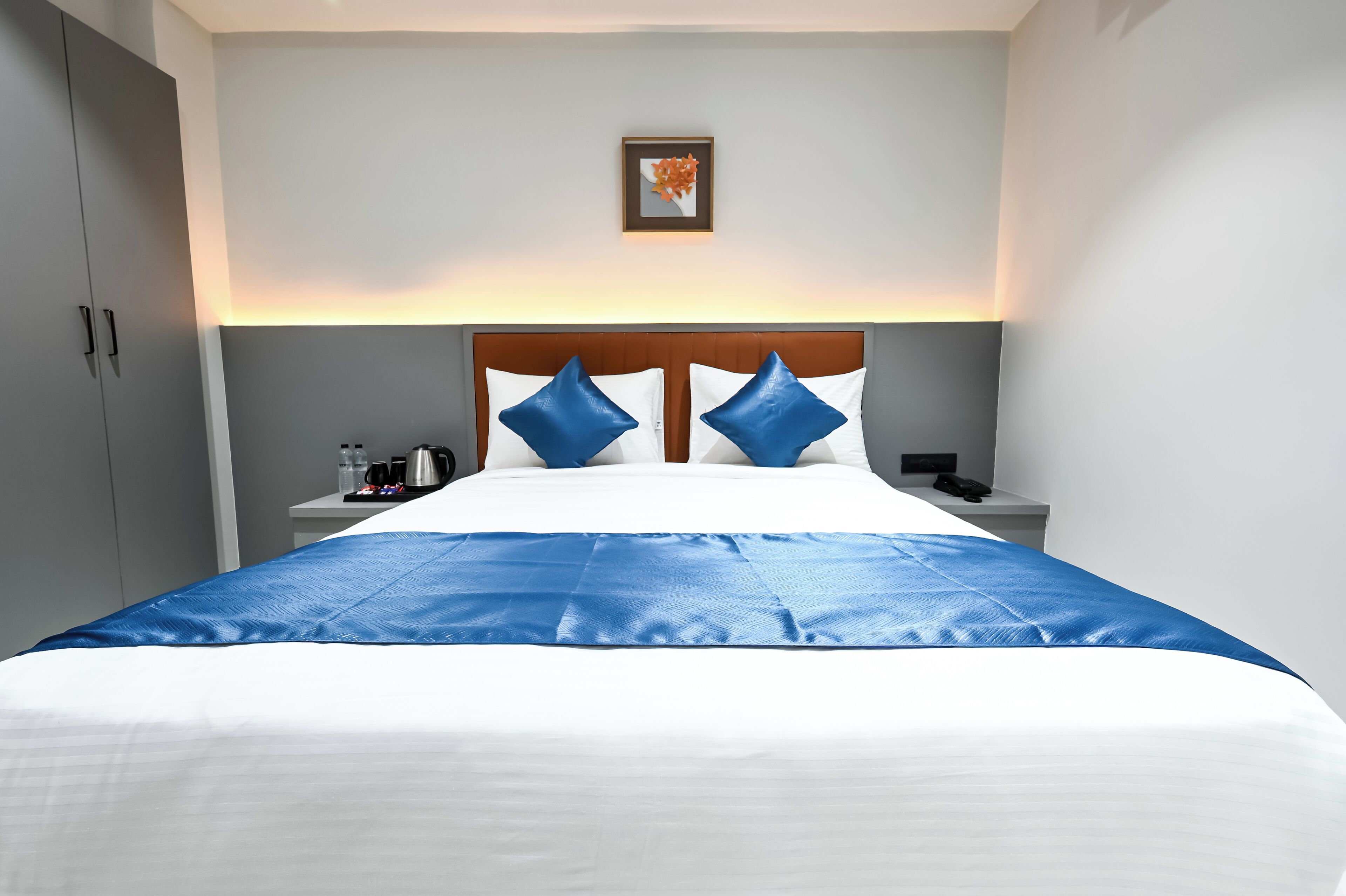 A hotel room with a bed, a nightstand, a coffee maker, and a framed picture on the wall.