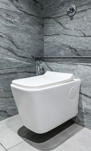 A modern bathroom with a white toilet, a wall-mounted faucet, and a marble-patterned wall. - Hotel Sun lorem, Ahmedabad (Ahmedabad)
