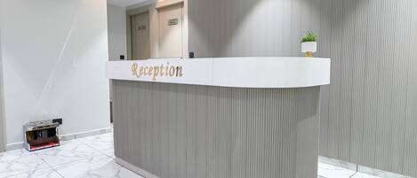 Un comptoir d’accueil avec une pancarte indiquant « Réception », une caméra de surveillance et une plante posée sur le dessus.