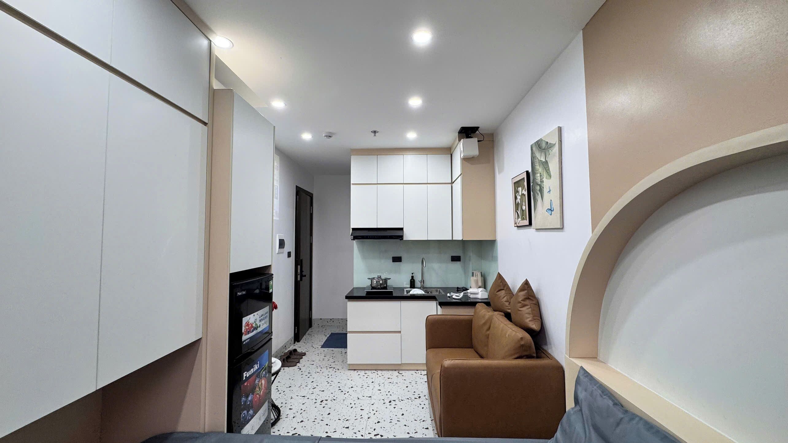 A compact kitchen with white cabinets, a black countertop, and a brown sofa.