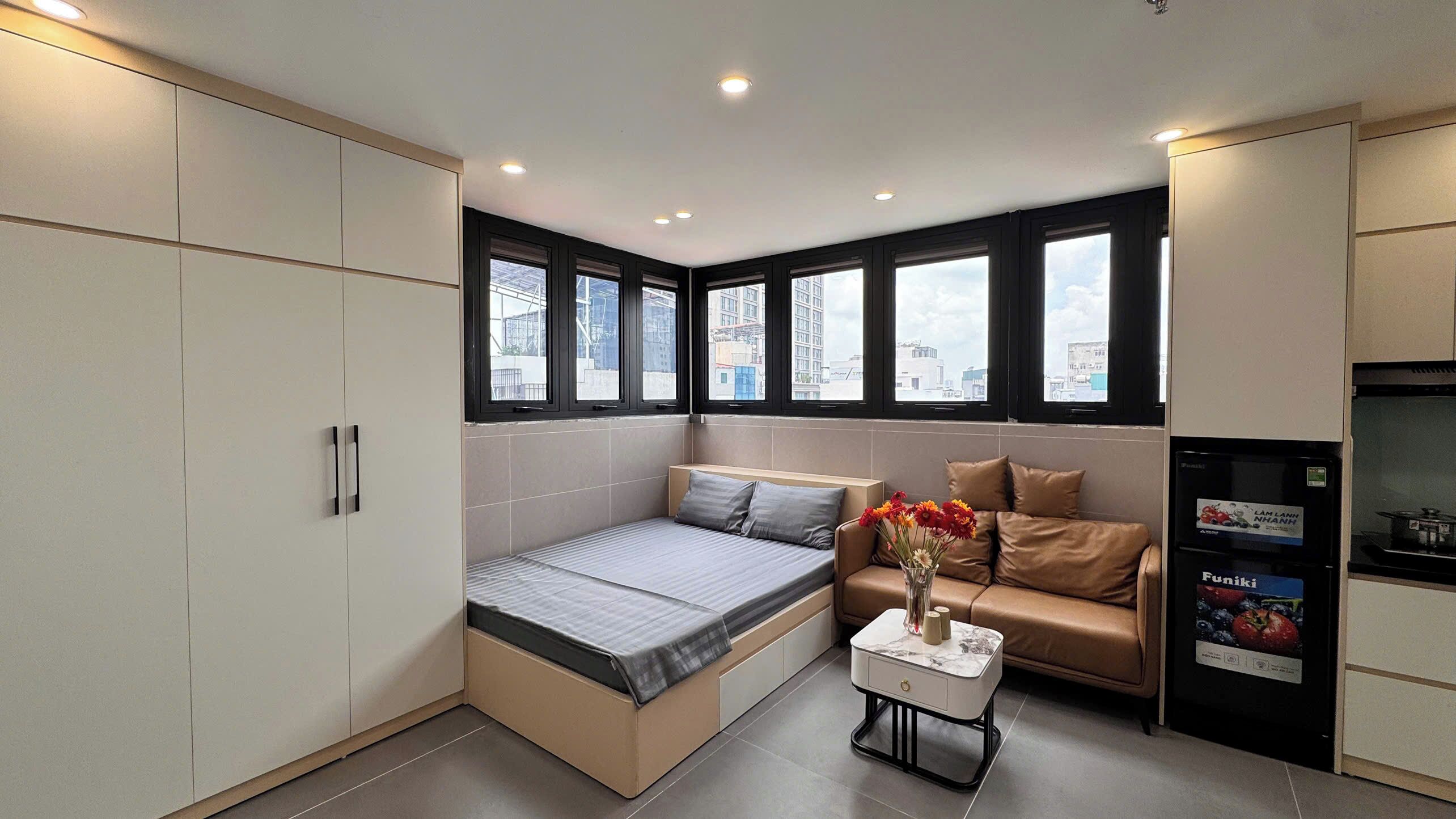 A compact room with a bed, a sofa, a small table, and a refrigerator.