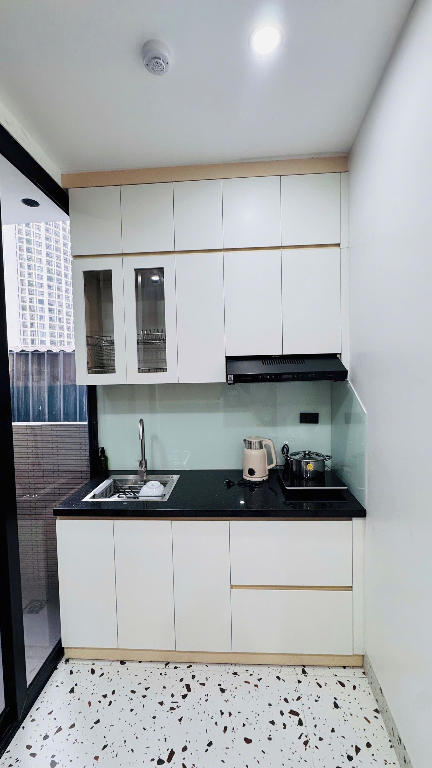 A compact kitchen with white cabinets, a black countertop, a stainless steel sink, and a black range hood.