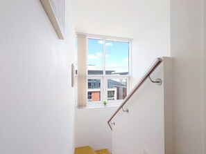 A staircase with a handrail leading to a window overlooking a building. - Two Bedroom Duplex Pent House in ExCeL (Greater London)