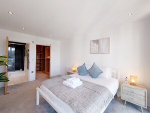 A modern bedroom with a large bed, bedside lamps, a wardrobe, and a view of the outside. - Two Bedroom Duplex Pent House in ExCeL (Greater London)
