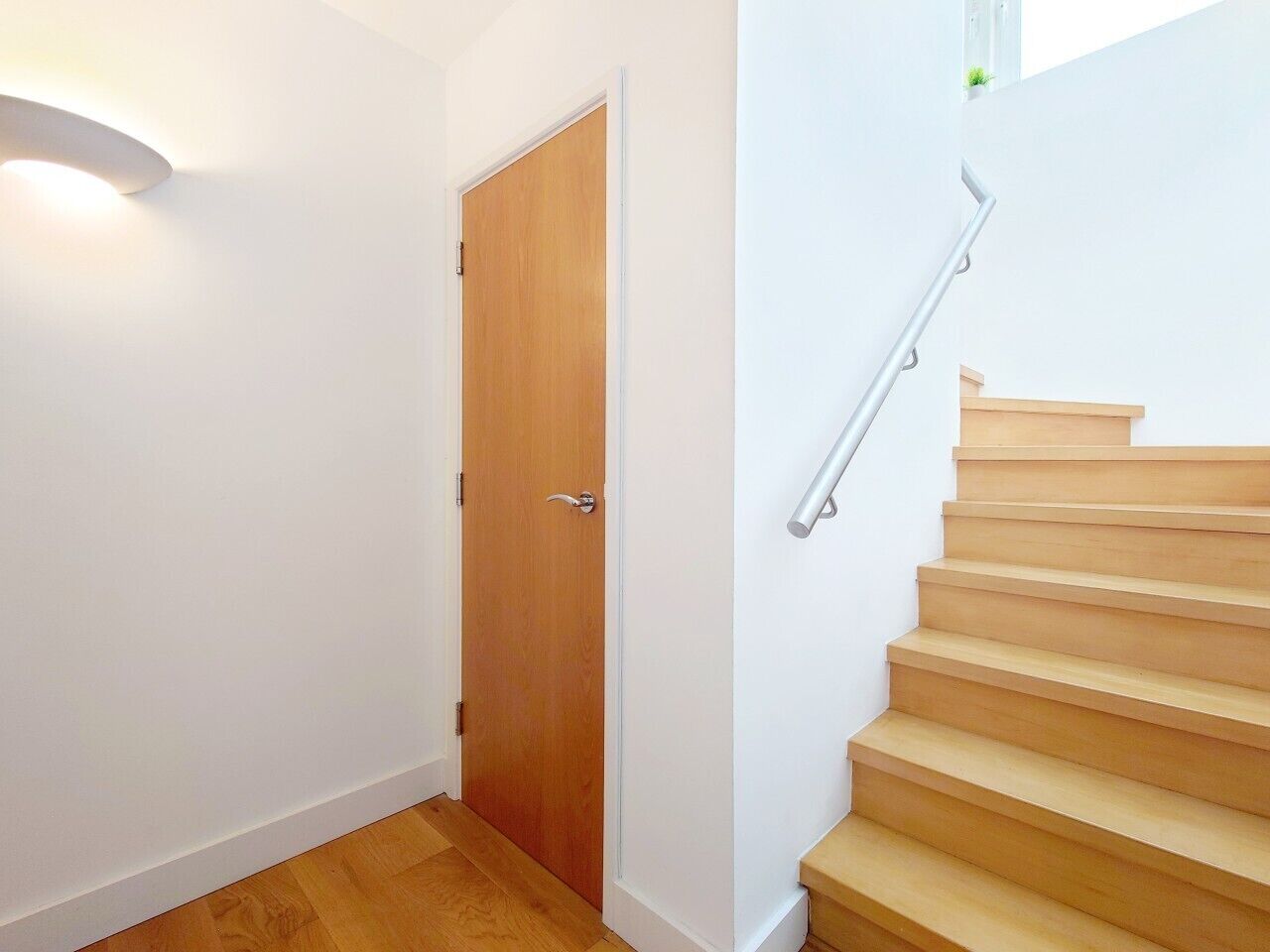 Eine Treppe mit Holzbodenstufen und einem Metallgeländer, die zu einer Holztür mit silbernem Drücker führt.