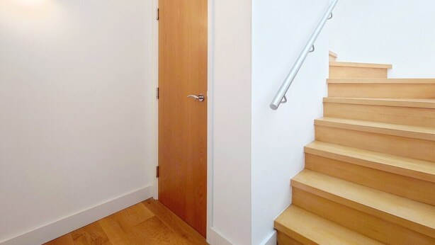 Una escalera con peldaños de madera y barandilla metálica, que conduce a una puerta de madera con picaporte plateado.