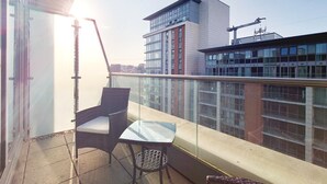 Un balcón con una silla y una mesa, con vistas a un paisaje urbano con edificios modernos.