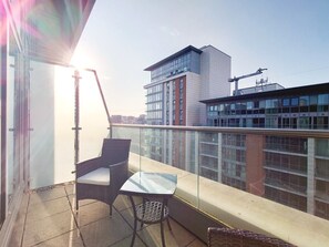 A balcony with a chair and table, overlooking a cityscape with modern buildings. - Two Bedroom Duplex Pent House in ExCeL (Greater London)